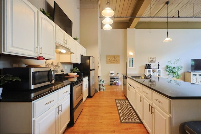 685 Social St Unit 103, Woonsocket, RI 02895 - kitchen featuring stainless steel appliances, a towering ceiling, under cabinet range hood, dark countertops, and white cabinetry