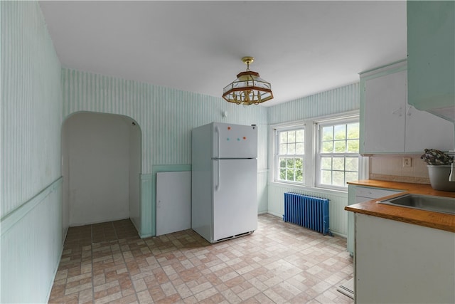 509 W Shore Rd, Warwick, RI 02889 - kitchen with freestanding refrigerator, radiator, wallpapered walls, and brick patterned flooring