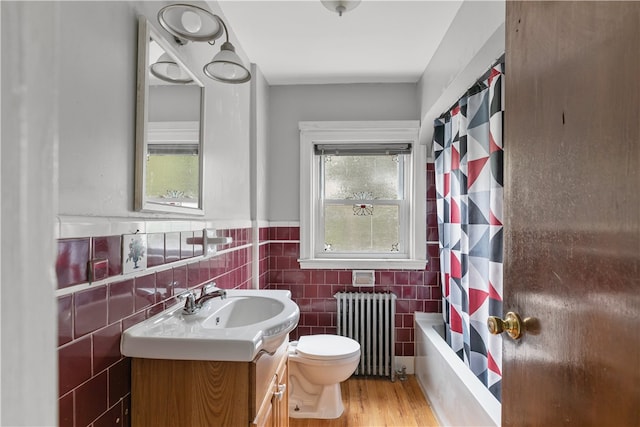 509 W Shore Rd, Warwick, RI 02889 - full bath with radiator heating unit, vanity, tile walls, wood finished floors, and shower / tub combo with curtain