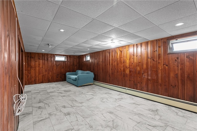 509 W Shore Rd, Warwick, RI 02889 - below grade area with a baseboard heating unit, healthy amount of natural light, wood walls, light marble finish flooring, and a paneled ceiling