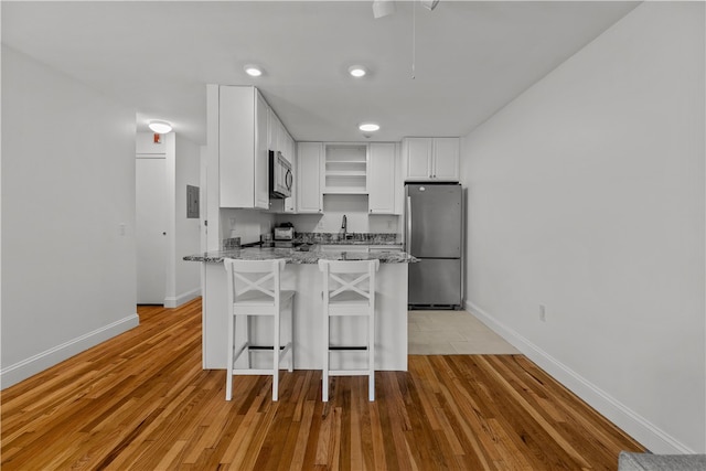 401 Bellevue Ave Unit 214, Newport, RI 02840 - kitchen featuring appliances with stainless steel finishes, open shelves, a peninsula, light stone counters, and white cabinetry