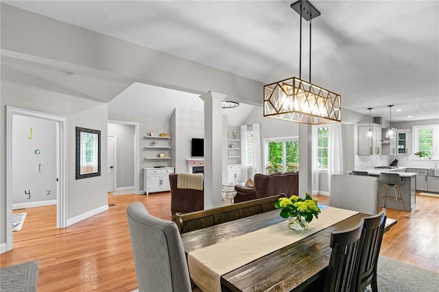 52 Pine Swamp Rd, Cumberland, RI 02864 - dining area with light wood-style floors, a fireplace, vaulted ceiling, built in shelves, and ornate columns