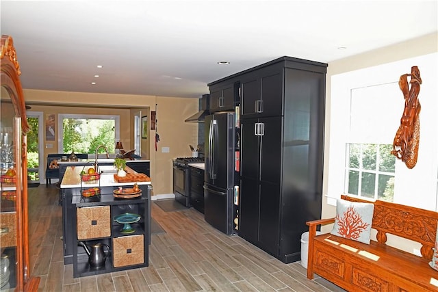 2352 Matunuck Schoolhouse Rd, Charlestown, RI 02813 - kitchen with black appliances, dark cabinetry, light countertops, light wood-style flooring, and an island with sink
