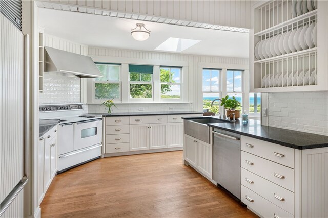 68 Grange Ave, Little Compton, RI 02837 - kitchen featuring electric range, wall chimney exhaust hood, stainless steel dishwasher, a skylight, and light wood-type flooring