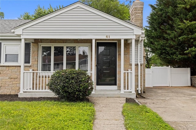 41 Valley View Dr, Cumberland, RI 02864 - doorway to property with stone siding, a chimney, a shingled roof, concrete driveway, and covered porch