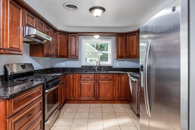 136 Davis Ave, Cranston, RI 02910 - kitchen featuring appliances with stainless steel finishes, under cabinet range hood, light tile patterned floors, dark stone counters, and brown cabinetry