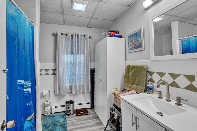 222 Pavilion Ave, Providence, RI 02905 - bathroom featuring a paneled ceiling, baseboard heating, vanity, tile walls, and wood finished floors