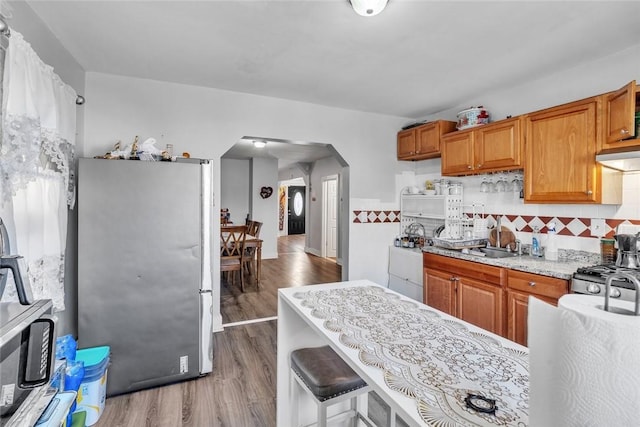 222 Pavilion Ave, Providence, RI 02905 - kitchen with freestanding refrigerator, arched walkways, wood finished floors, brown cabinets, and decorative backsplash