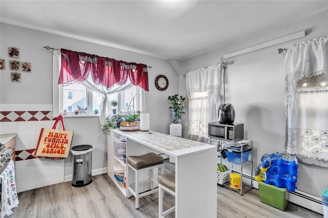 222 Pavilion Ave, Providence, RI 02905 - kitchen featuring stainless steel microwave, a baseboard heating unit, wood finished floors, and a breakfast bar