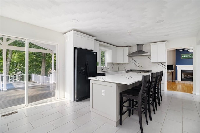 29 Gilcrest Dr, West Warwick, RI 02893 - kitchen featuring wall chimney range hood, black refrigerator with ice dispenser, a kitchen island, light tile patterned floors, and tasteful backsplash