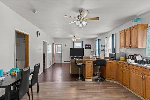 18 Ortoleva Dr, Providence, RI 02909 - kitchen featuring stainless steel microwave, a ceiling fan, wood finished floors, a peninsula, and brown cabinetry