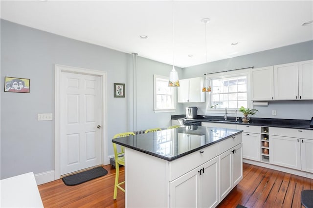 6 Pond Ave, Newport, RI 02840 - kitchen with dark countertops, dark wood-style floors, white cabinets, a breakfast bar area, and decorative light fixtures