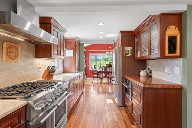 12 Windward Cir, Warwick, RI 02889 - kitchen with stainless steel appliances, wall chimney exhaust hood, a chandelier, glass insert cabinets, and backsplash