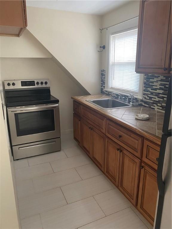 26 Anchor St, Providence, RI 02908 - kitchen featuring electric stove, tile counters, brown cabinetry, light tile patterned flooring, and decorative backsplash