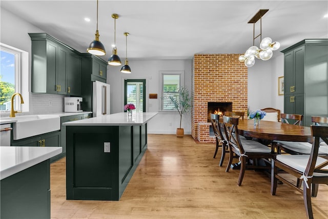 93 E Main Rd, Portsmouth, RI 02871 - kitchen with green cabinetry, light countertops, light wood finished floors, a brick fireplace, and a kitchen island