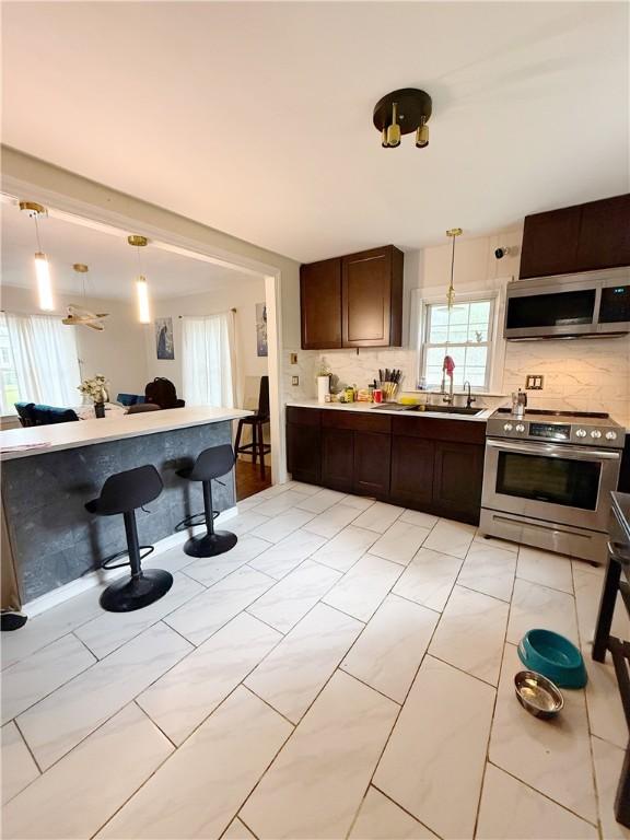 26 Westmore St, Providence, RI 02910 - kitchen featuring appliances with stainless steel finishes, decorative backsplash, dark brown cabinets, pendant lighting, and light countertops