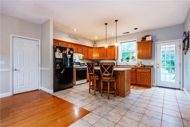 50 S Pond Dr, Coventry, RI 02816 - kitchen with black fridge, white gas range, under cabinet range hood, a breakfast bar area, and brown cabinetry