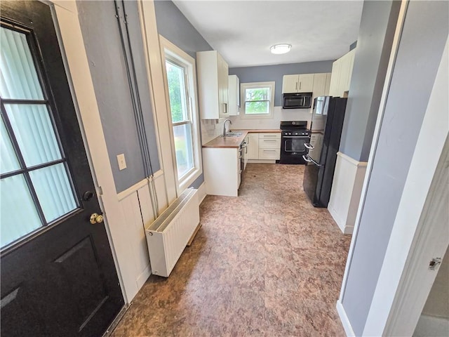156 Broad St, Burrillville, RI 02859 - kitchen with radiator heating unit, black appliances, wainscoting, white cabinets, and light countertops