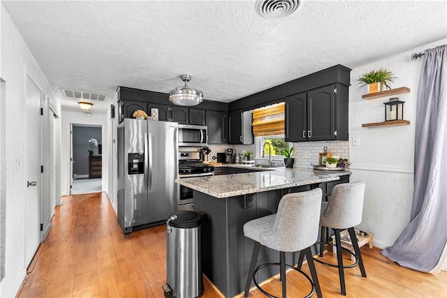 59 Columbus Ave, North Providence, RI 02911 - kitchen featuring appliances with stainless steel finishes, a peninsula, light wood-type flooring, a kitchen bar, and light stone countertops