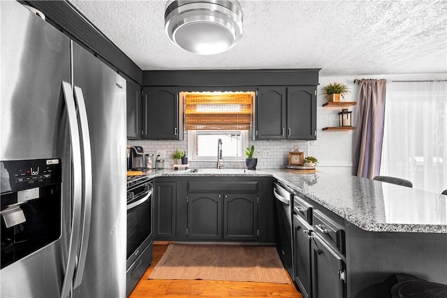 59 Columbus Ave, North Providence, RI 02911 - kitchen with appliances with stainless steel finishes, a textured ceiling, a peninsula, backsplash, and light wood-type flooring