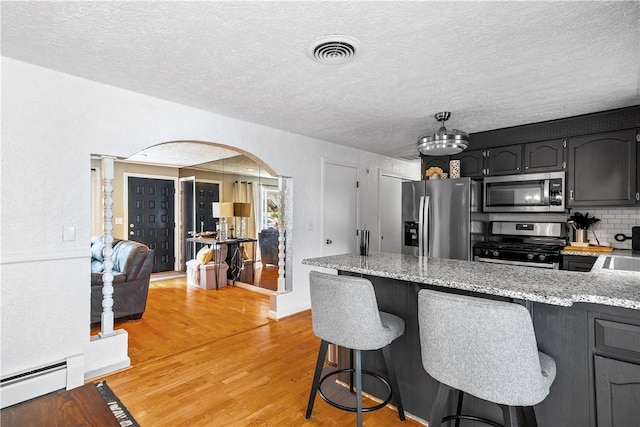 59 Columbus Ave, North Providence, RI 02911 - kitchen featuring stainless steel appliances, baseboard heating, arched walkways, light wood finished floors, and a breakfast bar area