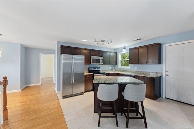 22 Riverdale Rd, Westerly, RI 02891 - kitchen featuring appliances with stainless steel finishes, dark brown cabinets, a kitchen bar, light stone counters, and a kitchen island