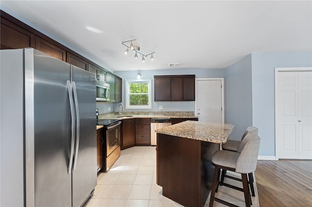22 Riverdale Rd, Westerly, RI 02891 - kitchen featuring stainless steel appliances, a center island, a breakfast bar area, dark brown cabinetry, and light stone counters