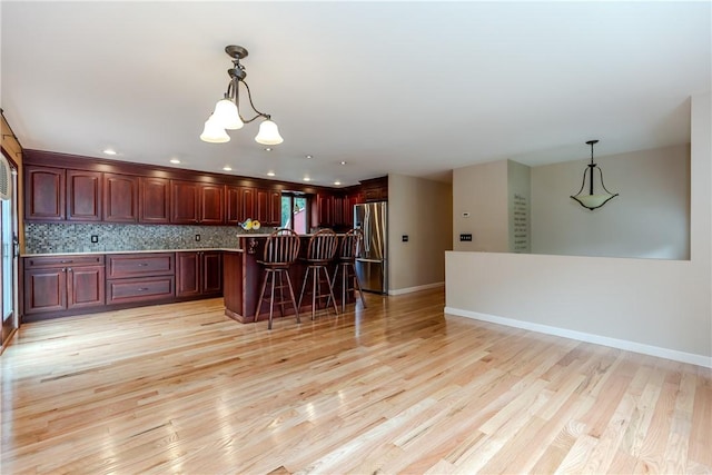 422 Buxton St, North Smithfield, RI 02896 - kitchen featuring freestanding refrigerator, reddish brown cabinets, light wood-type flooring, hanging light fixtures, and a kitchen breakfast bar