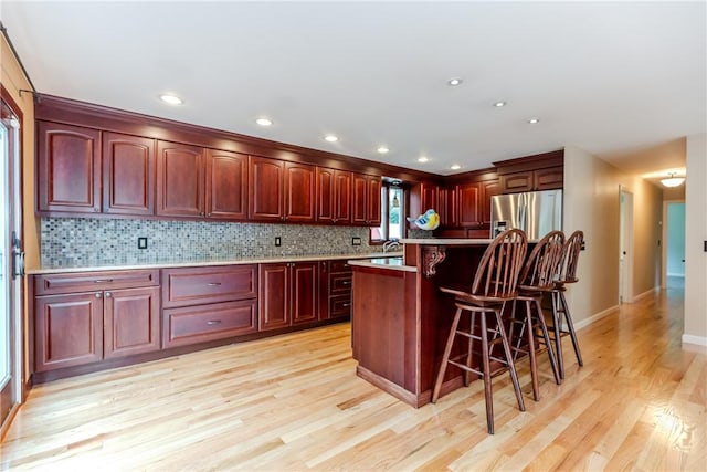 422 Buxton St, North Smithfield, RI 02896 - kitchen with dark brown cabinets, stainless steel fridge with ice dispenser, a kitchen breakfast bar, light wood finished floors, and backsplash