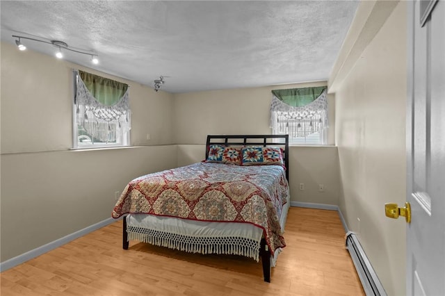 203 Pulaski St, West Warwick, RI 02893 - bedroom with wood finished floors, a baseboard heating unit, a textured ceiling, and track lighting