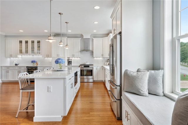 100 Algonquin Rd Unit 13, Narragansett, RI 02882 - kitchen with wall chimney range hood, stainless steel appliances, a breakfast bar area, light wood-style flooring, and white cabinetry