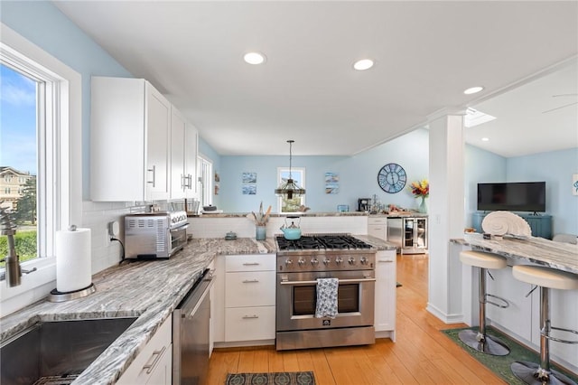 408 Atlantic Ave, Westerly, RI 02891 - kitchen featuring stainless steel appliances, a peninsula, light stone counters, white cabinetry, and light wood-style floors