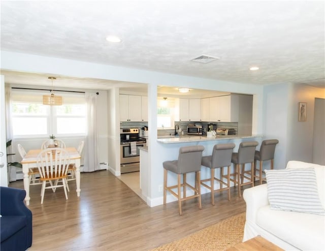 94 Osage Dr, Warwick, RI 02888 - kitchen featuring appliances with stainless steel finishes, a breakfast bar, light wood finished floors, white cabinets, and light countertops