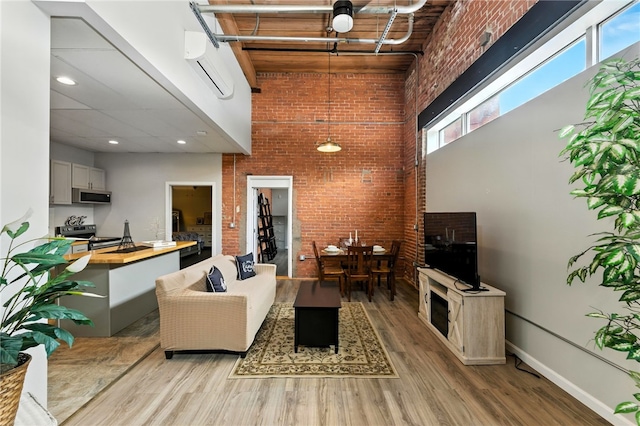 1117 Douglas Ave Unit 124, North Providence, RI 02904 - living room featuring brick wall, a high ceiling, a wall mounted air conditioner, and light wood-style flooring