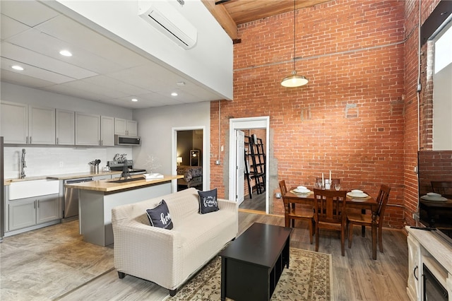 1117 Douglas Ave Unit 124, North Providence, RI 02904 - living room with a wall mounted AC, brick wall, light wood finished floors, and a towering ceiling