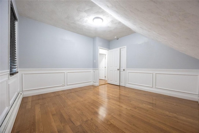 193 Howell St Unit 3, Providence, RI 02906 - additional living space featuring baseboard heating, wood finished floors, a textured ceiling, vaulted ceiling, and a wainscoted wall