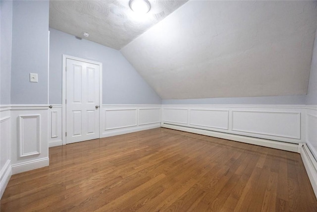 193 Howell St Unit 3, Providence, RI 02906 - bonus room featuring a decorative wall, vaulted ceiling, a baseboard heating unit, wood finished floors, and wainscoting