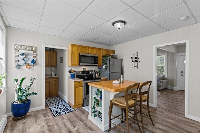 57 Maple Ave, Johnston, RI 02919 - kitchen with stainless steel appliances, light wood-style floors, a paneled ceiling, a baseboard radiator, and a breakfast bar