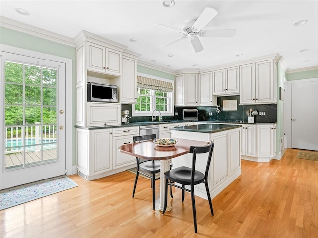 173 Gaskill St, Woonsocket, RI 02895 - kitchen with stainless steel microwave, dark countertops, light wood-type flooring, tasteful backsplash, and ornamental molding