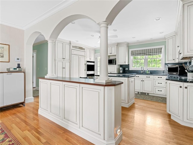 173 Gaskill St, Woonsocket, RI 02895 - kitchen featuring a kitchen island, ornate columns, dark countertops, light wood-type flooring, and crown molding