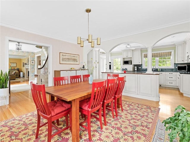 173 Gaskill St, Woonsocket, RI 02895 - dining space with light wood-type flooring, arched walkways, crown molding, and ornate columns