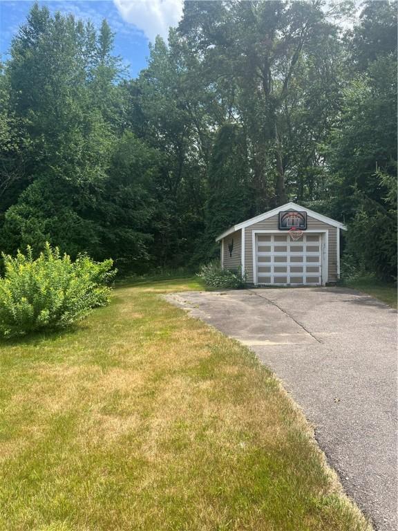 354 Rhodes Ave, Woonsocket, RI 02895 - view of grassy yard featuring an outdoor structure, driveway, a detached garage, and a forest view