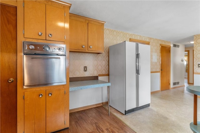 352 Cove Ave, Warwick, RI 02886 - kitchen with freestanding refrigerator, oven, wallpapered walls, and brown cabinetry