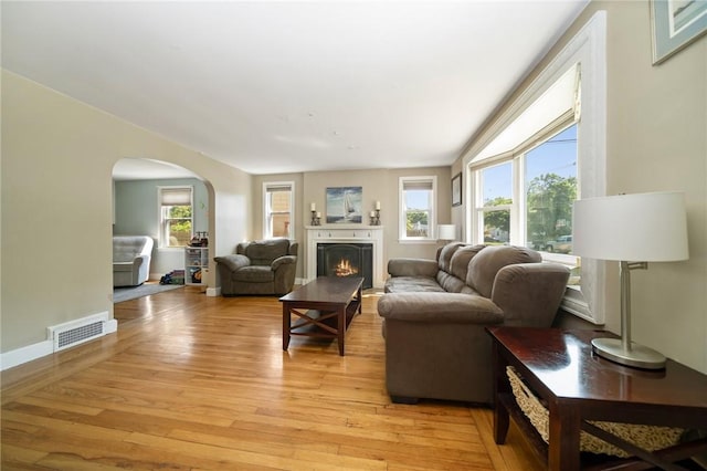79 Pilgrim Dr, Warwick, RI 02888 - living room with arched walkways, light wood-style floors, and a warm lit fireplace