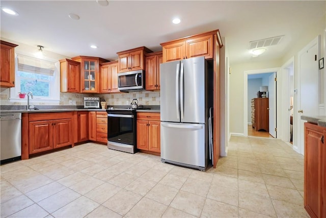 72 Audubon Rd, Warwick, RI 02888 - kitchen featuring stainless steel appliances, brown cabinets, tasteful backsplash, light tile patterned floors, and glass insert cabinets
