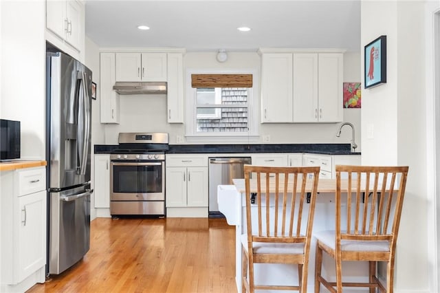 92 Franklin St, Bristol, RI 02809 - kitchen with appliances with stainless steel finishes, under cabinet range hood, white cabinetry, light wood-type flooring, and dark countertops