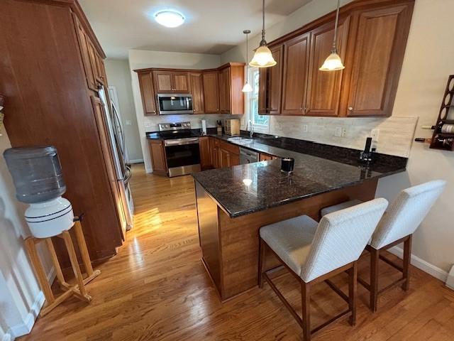 75 Lauriston St, Providence, RI 02906 - kitchen with stainless steel appliances, a peninsula, brown cabinetry, and light wood-style floors