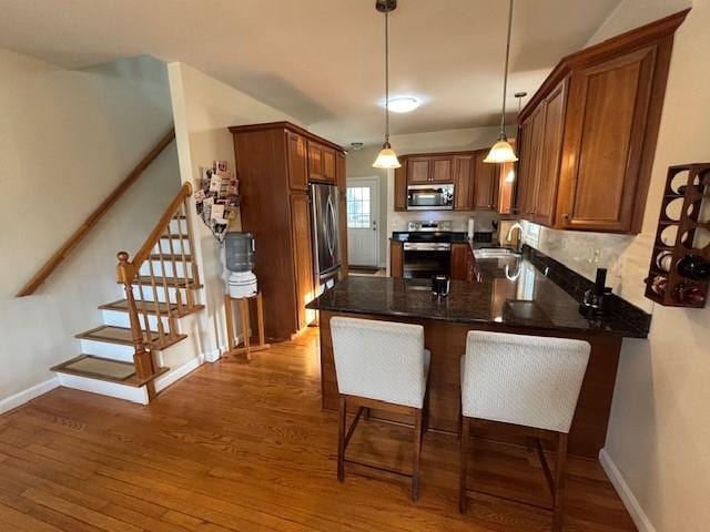 75 Lauriston St, Providence, RI 02906 - kitchen featuring stainless steel appliances, a peninsula, wood finished floors, decorative light fixtures, and brown cabinets