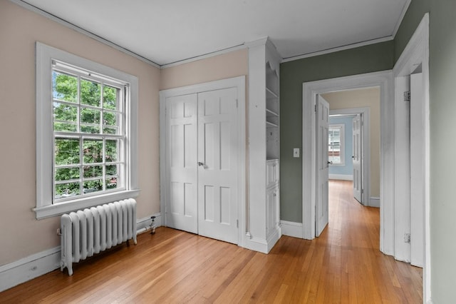 189 Butler Ave, Providence, RI 02906 - unfurnished bedroom with radiator heating unit, multiple windows, light wood-style flooring, ornamental molding, and a closet