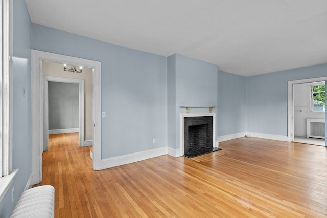189 Butler Ave, Providence, RI 02906 - unfurnished living room featuring radiator, a fireplace with flush hearth, light wood-type flooring, and a chandelier